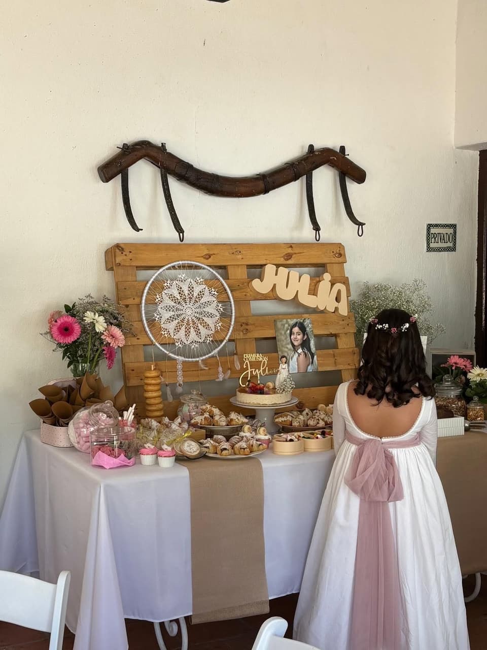 Niña vestida de comunión delante de su mesa dulce